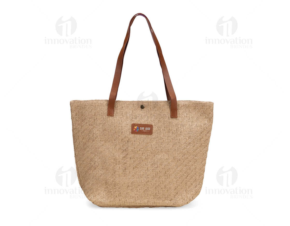 Bolsa confeccionada em palha trançada com fechamento em botão metálico de pressão. Possui revestimento interno em algodão e bolso com fechamento em zíper, além de alças e plaqueta frontal em couro sintético.