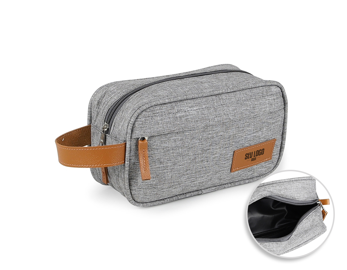 Necessaire confeccionada em poliéster com detalhes em couro sintético, possui dois compartimentos com zíper, alça para transporte e alça pequena para acesso de chaveiro ou gancho.